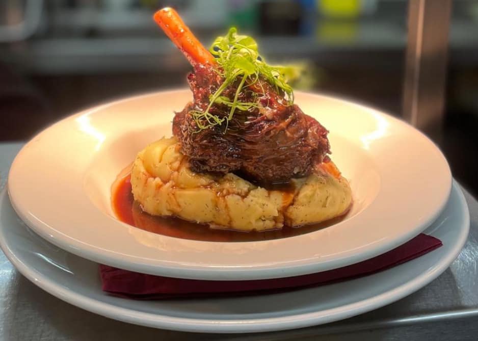 Slow-braised lamb shank on creamy mash with rich gravy and a single carrot garnish — a pub classic from The George's kitchen