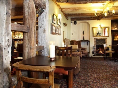 Inside The George Inn — exposed timber beams, fireside armchair and a lit candle on a heavy wooden table