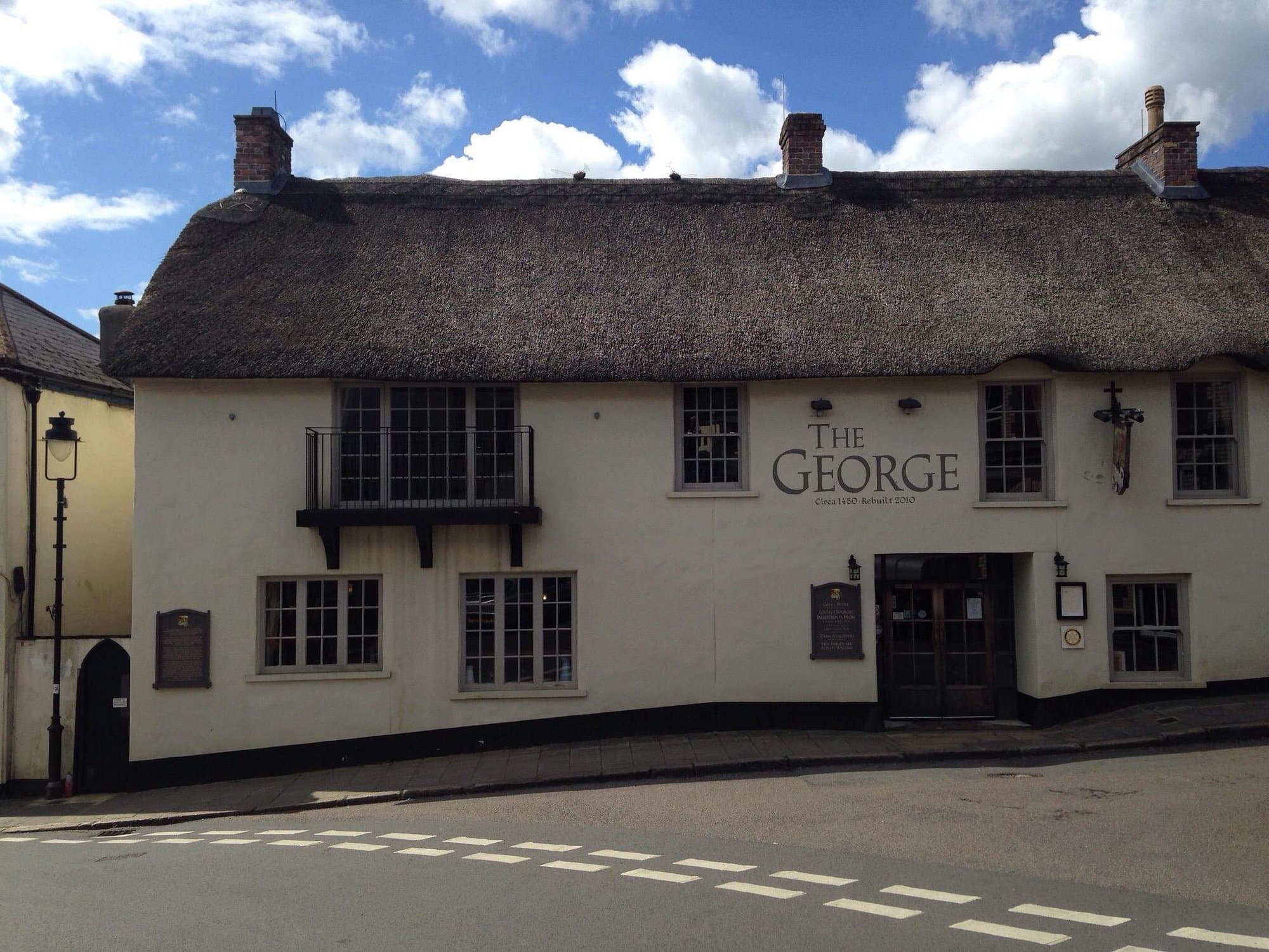 The George Inn — white-painted thatched-roof facade with the painted THE GEORGE · Circa 1450 · Rebuilt 2010 wall sign, Market Street, Hatherleigh, Devon