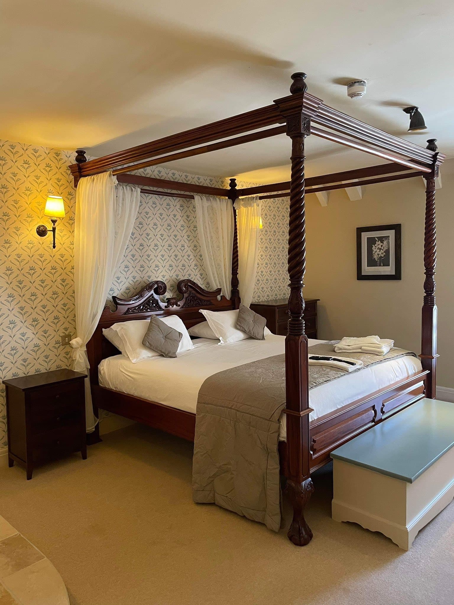 Mahogany four-poster with white voile drapes, carved finials and patterned cream wallpaper — a Superior Four-Poster room at The George Inn